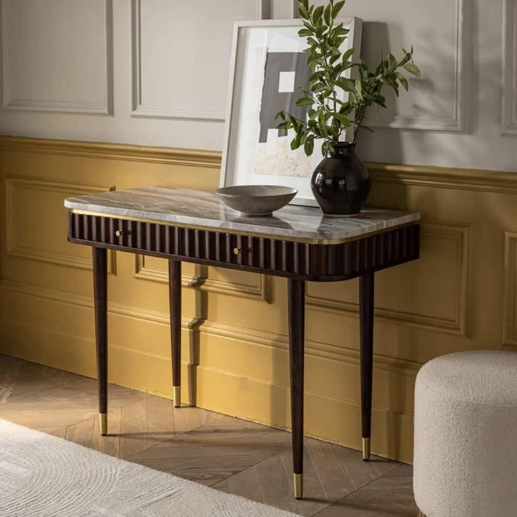 Modern console table against mustard colour wall panelling, styled with a black vase, framed artwork and brass accents.