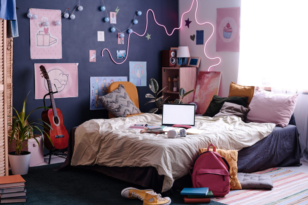 Modern teenage bedroom with a navy blue feature wall, adorned with neon lights, posters, and fairy lights. A creative and personalised space with eclectic decor and cosy textiles.