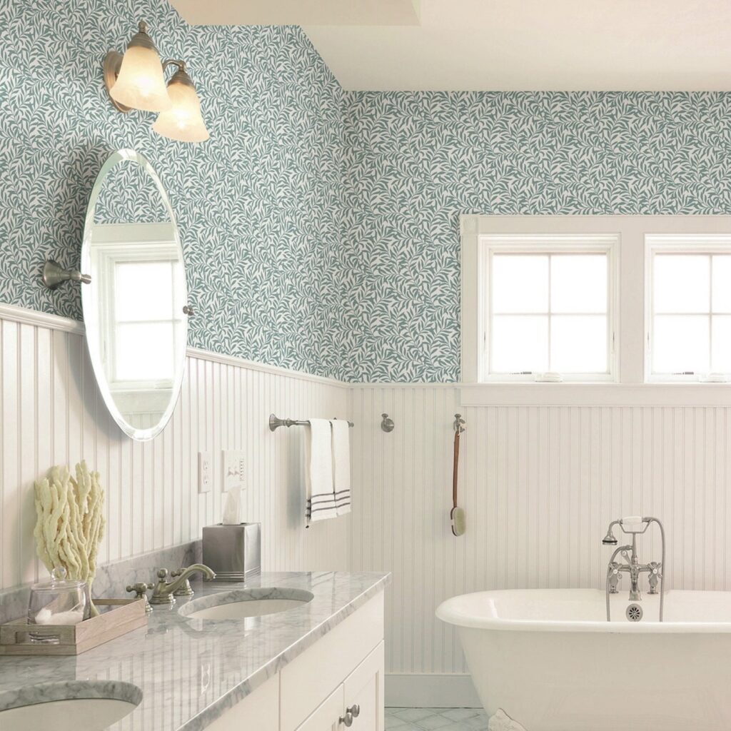 Teal leaf peel-and-stick wallpaper above white beadboard panelling in a classic bathroom with freestanding bath and oval mirror — budget small bathroom ideas UK