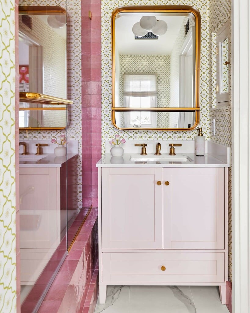 Pale pink painted bathroom vanity with brass hardware and patterned wallpaper