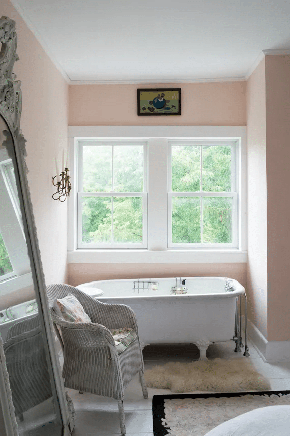 Pink Ground bathroom with a worn roll-top bath, wicker chair and gilt mirror