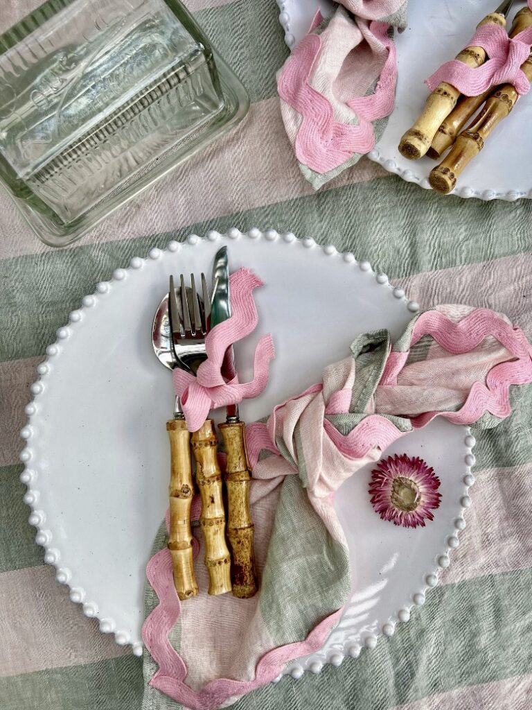 Spring table setting with bamboo cutlery, white beaded-edge plate, and pastel striped napkin from PoppyandHonesty on a pink and green linen tablecloth.