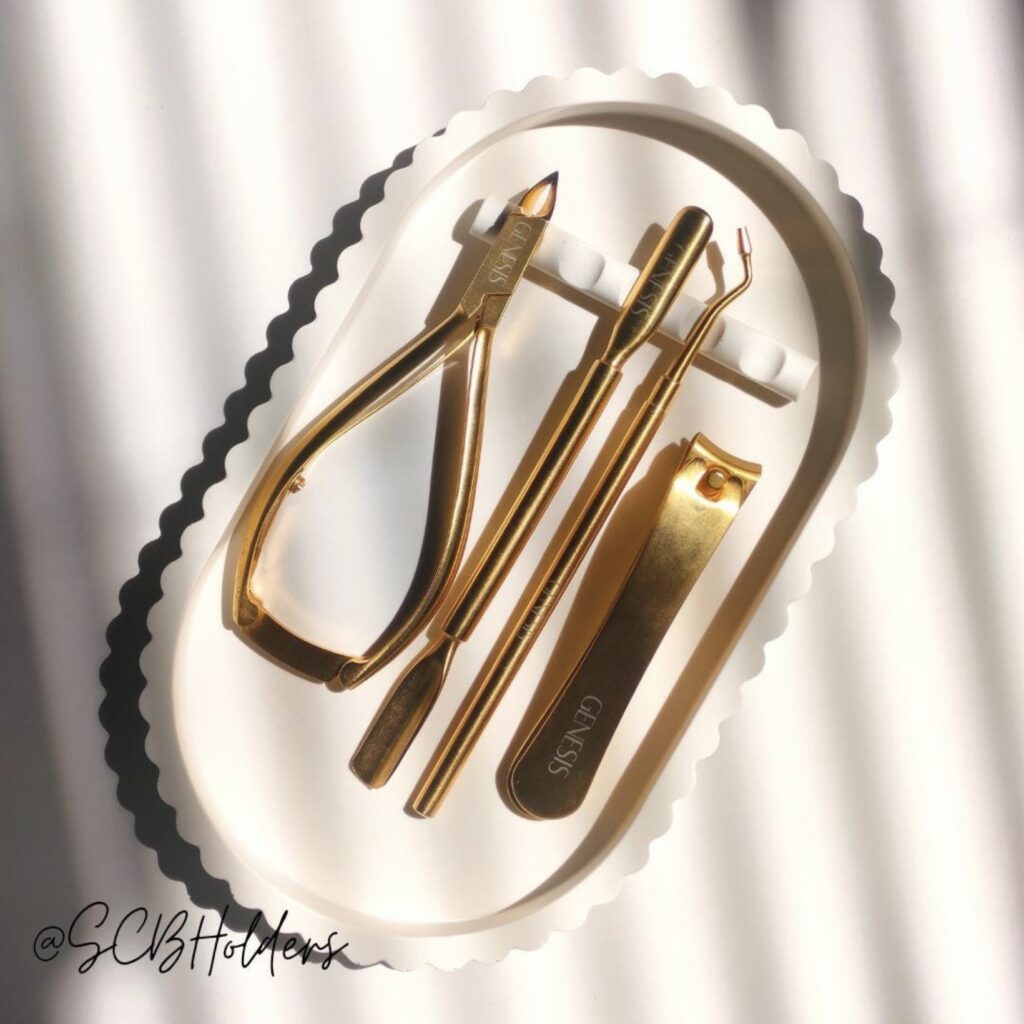 Scalloped-edge manicure tray holding gold nail tools, photographed in soft striped light.