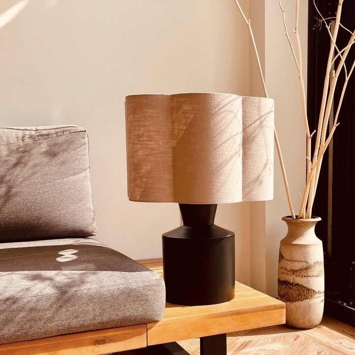 Scalloped edge table lamp with a light fabric shade on a side table beside a sofa, creating a warm, cosy glow.