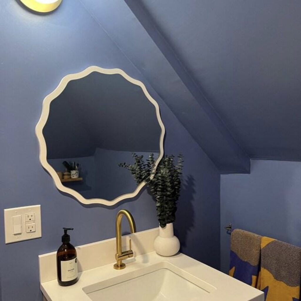 Scalloped edge round mirror above a white basin with brass tap in a blue cloakroom bathroom.