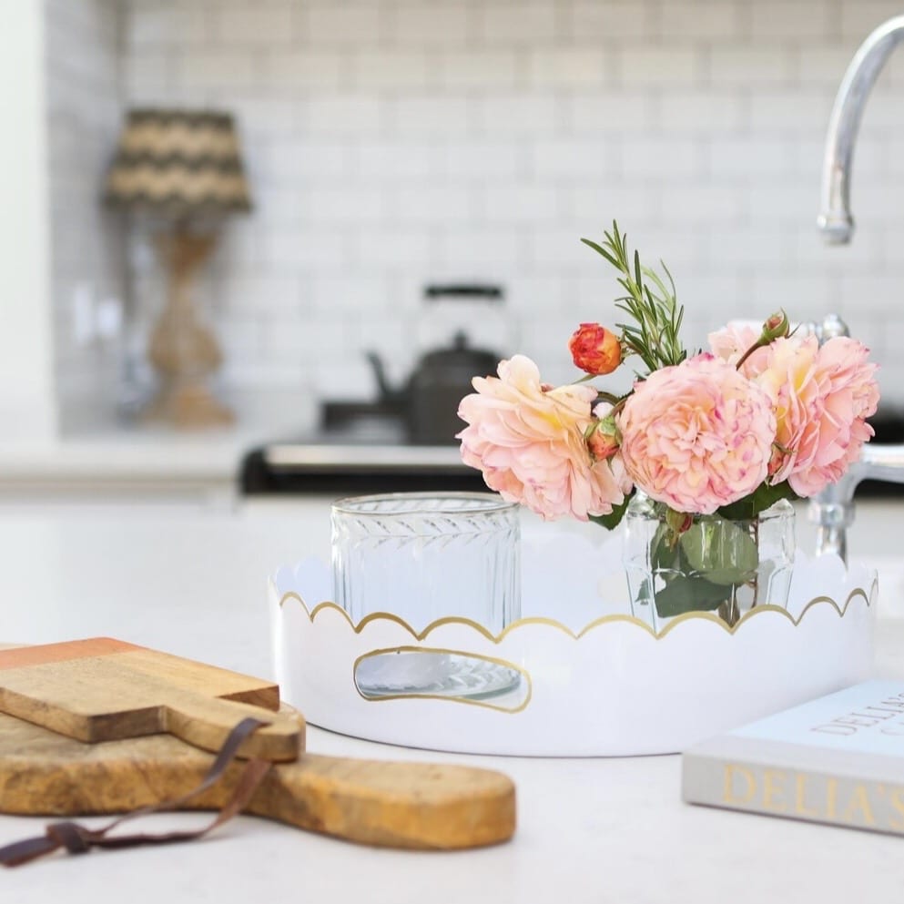White scalloped-edge serving tray with gold detailing, styled on a kitchen island with flowers and glassware.