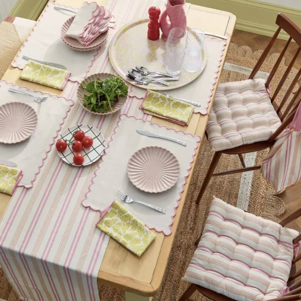 Pastel spring table setting with pink scalloped placemats, striped table runner and green napkins.