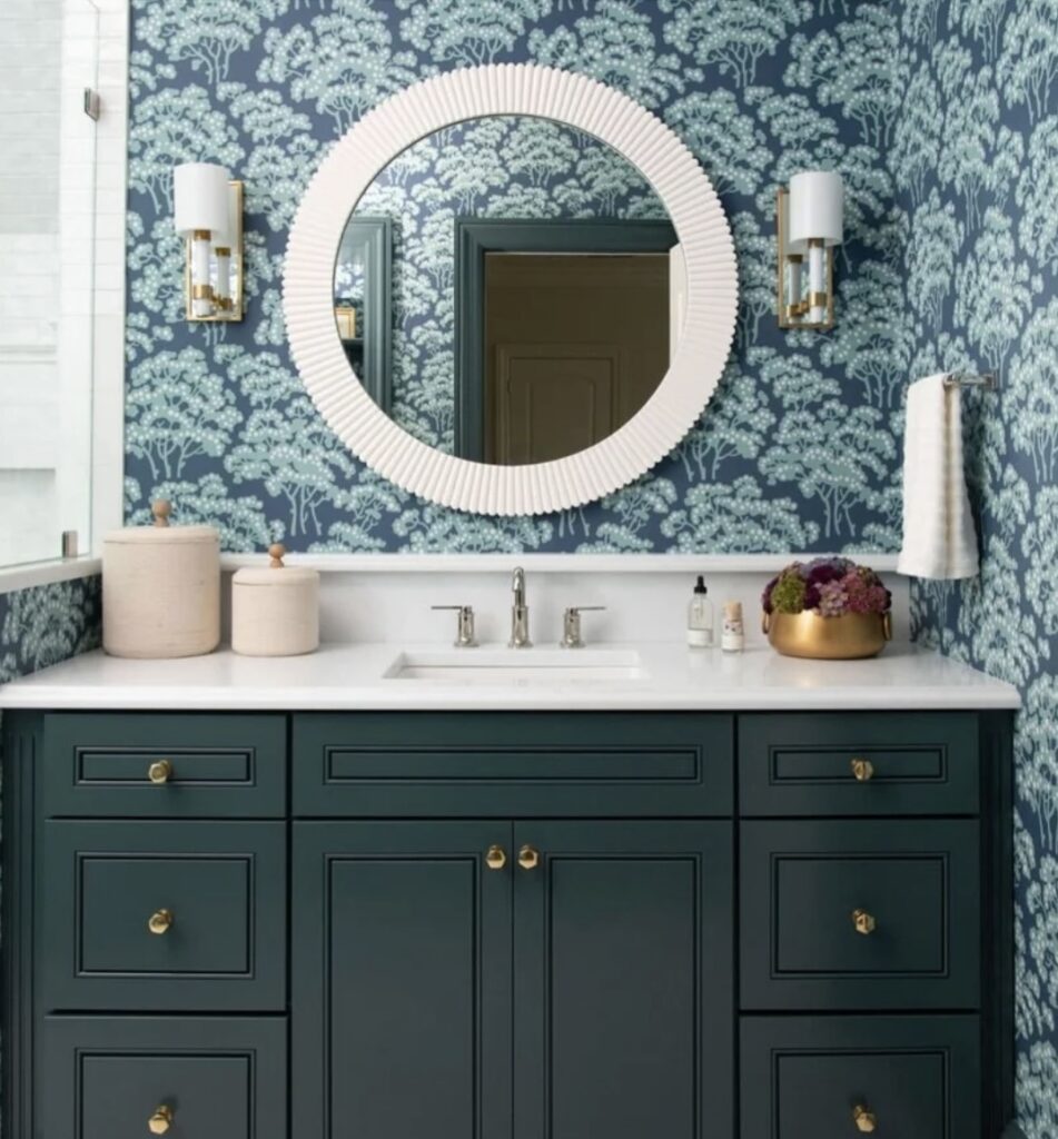 Green floral wallpaper behind round mirror and dark green vanity in a modern bathroom.