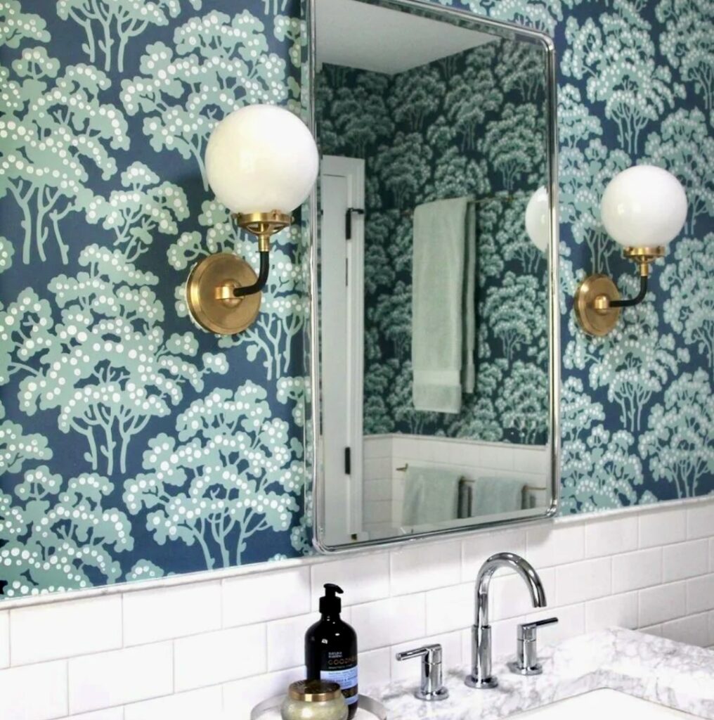 Bold green floral wallpaper in a modern bathroom with brass sconces and white subway tiles.