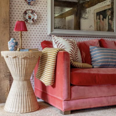 Scalloped rattan side table beside red velvet sofa with artisan decor and patterned cushions