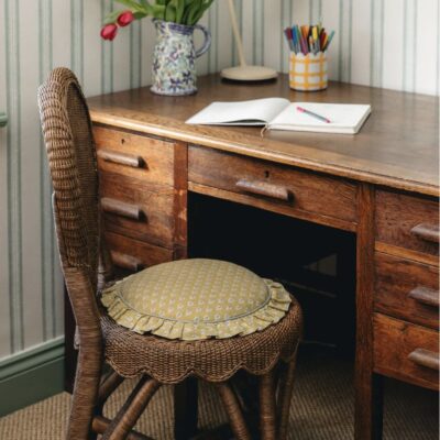 Vintage wooden desk with artisan wicker chair and frilled seat cushion in a home office setting