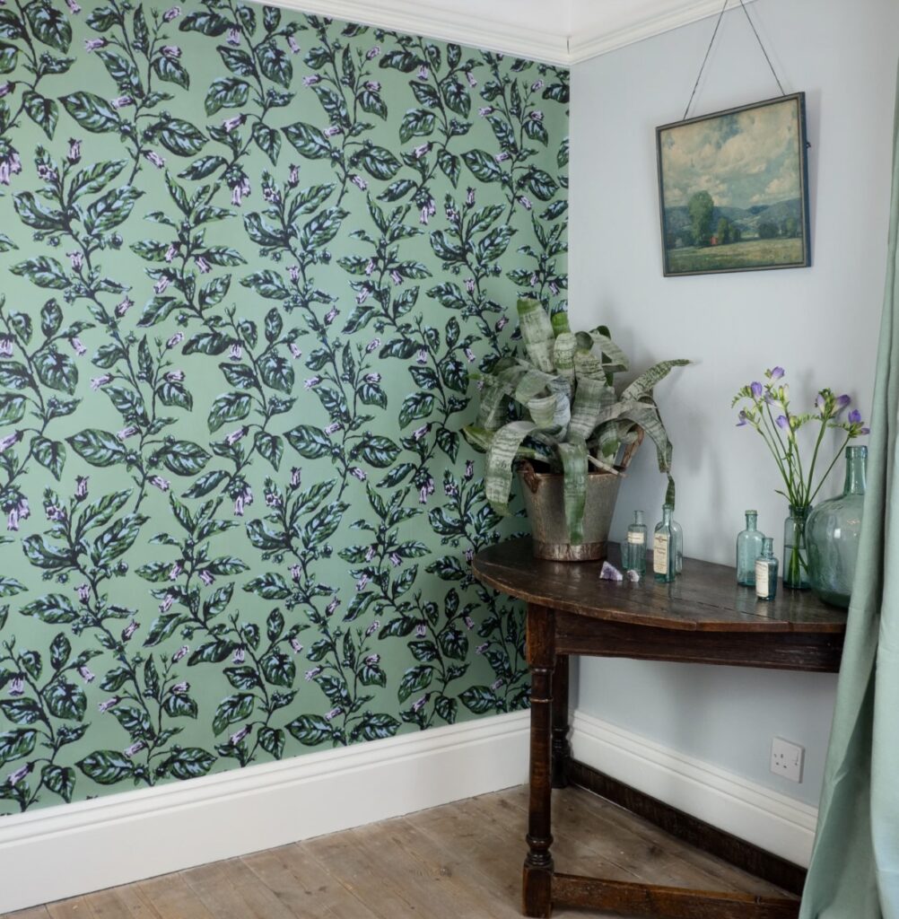 From Traditional to Bold: How to Decorate with Green Floral Wallpaper Screenshot 2025 06 30 at 09.54.27 Green floral wallpaper with rustic wood table and vintage green glass bottles.