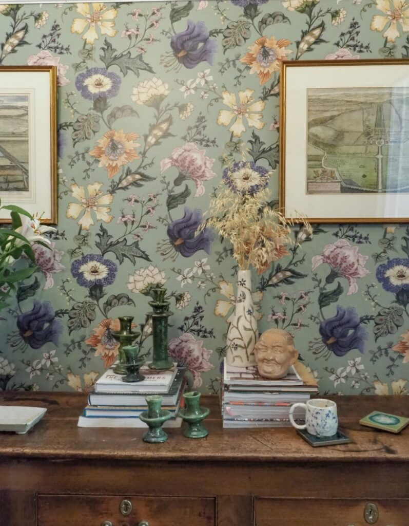 Bold green floral wallpaper with vintage console and eclectic decor in a hallway.