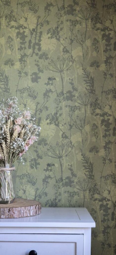 Green floral wallpaper with delicate botanical silhouettes styled with a white chest and dried flower arrangement.