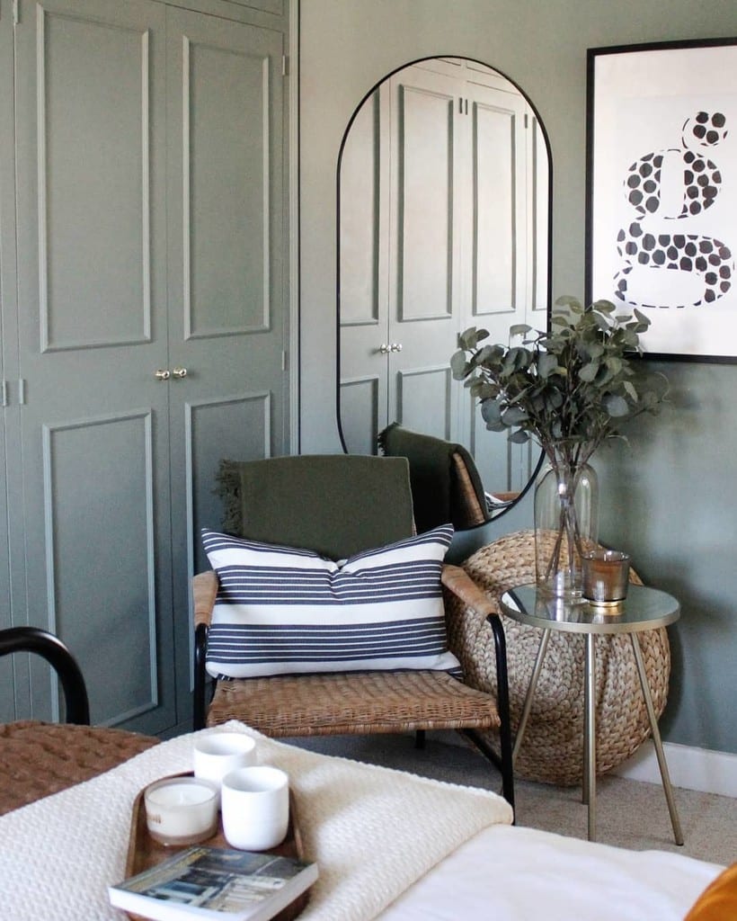 Budget bedroom ideas: secondhand bedroom corner with rattan armchair arch mirror and eucalyptus in Farrow and Ball Card Room Green @designseedandco_ltd