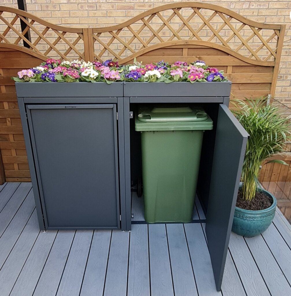 Grey metal wheelie bin storage with floral green roof and open bin door – modern and decorative wheelie bin storage idea