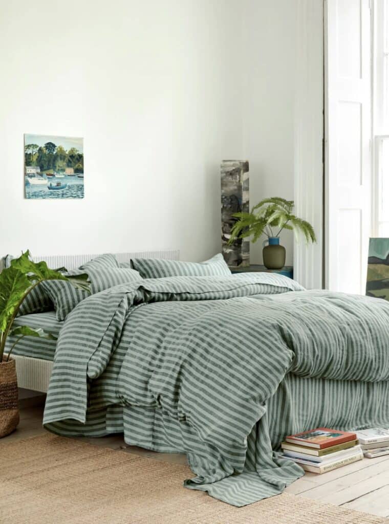 Sea-glass green striped bedding in a light-filled coastal bedroom with plants and jute rug