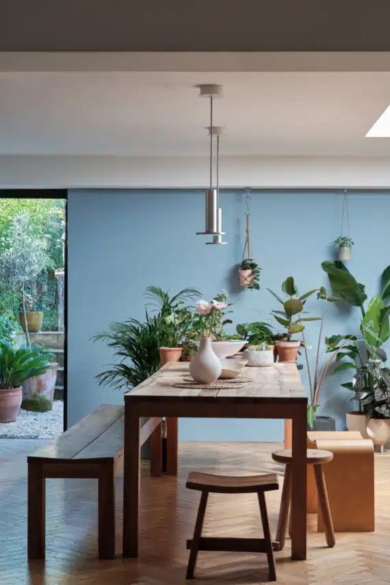 Lulworth Blue dining room with dark wood table, hanging plants and garden views — Farrow & Ball No. 89. Image credit: Farrow & Ball.