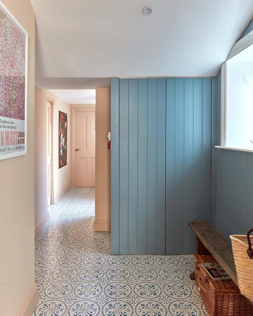 Hallway featuring Farrow & Ball Pink Ground walls, Selvedge blue panelling, patterned blue and white floor tiles, and a rustic wooden bench with baskets.