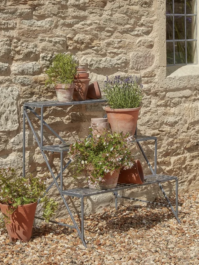Cox & Cox tiered metal plant stand styled with terracotta pots and herbs on a gravel garden – gravel garden ideas with pots
