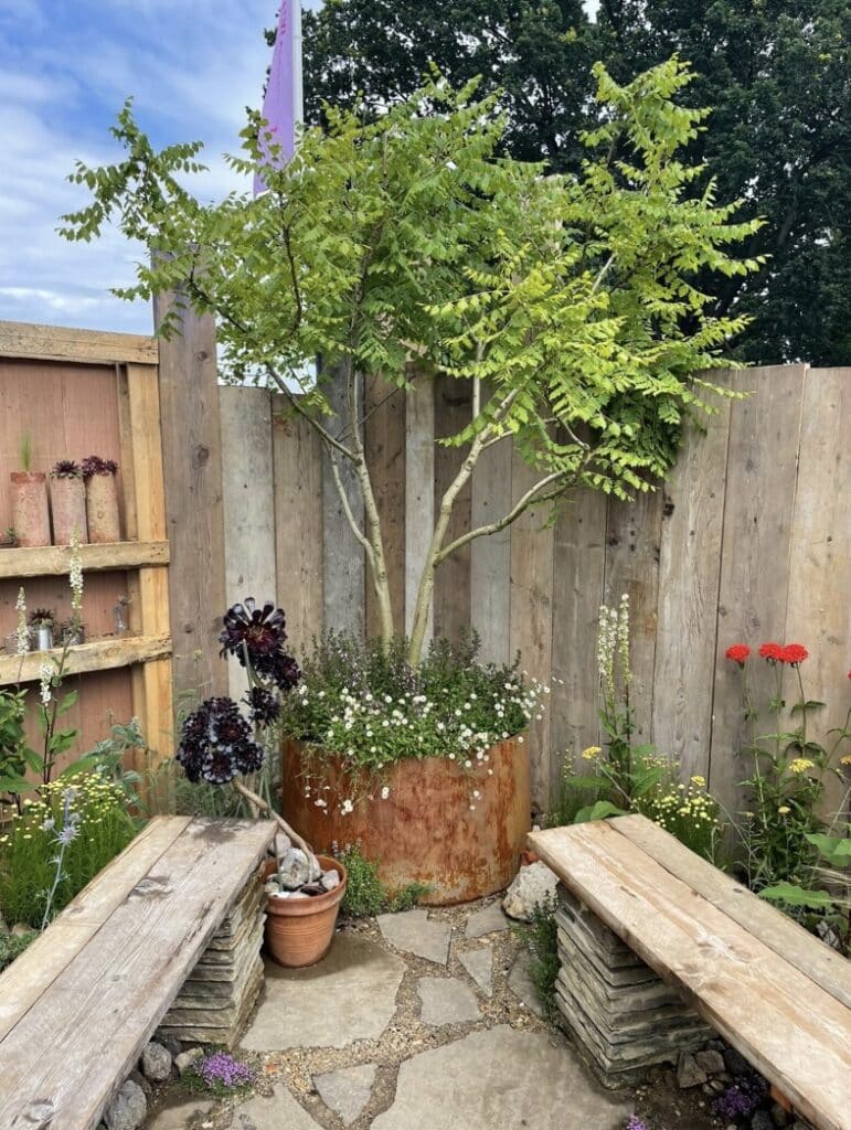 Small courtyard garden ideas with a weathered steel pot planter and bench seating — a calm gravel gardens with pots layout with Japanese plants outdoor.