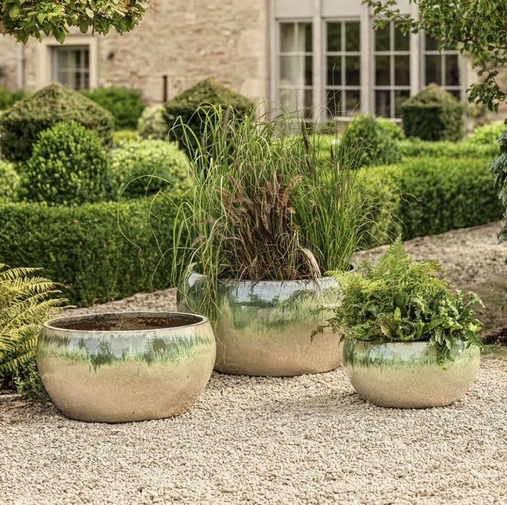 Glazed bowl planters grouped on pale gravel in a formal garden setting, showing an easy way to arrange pots on gravel.