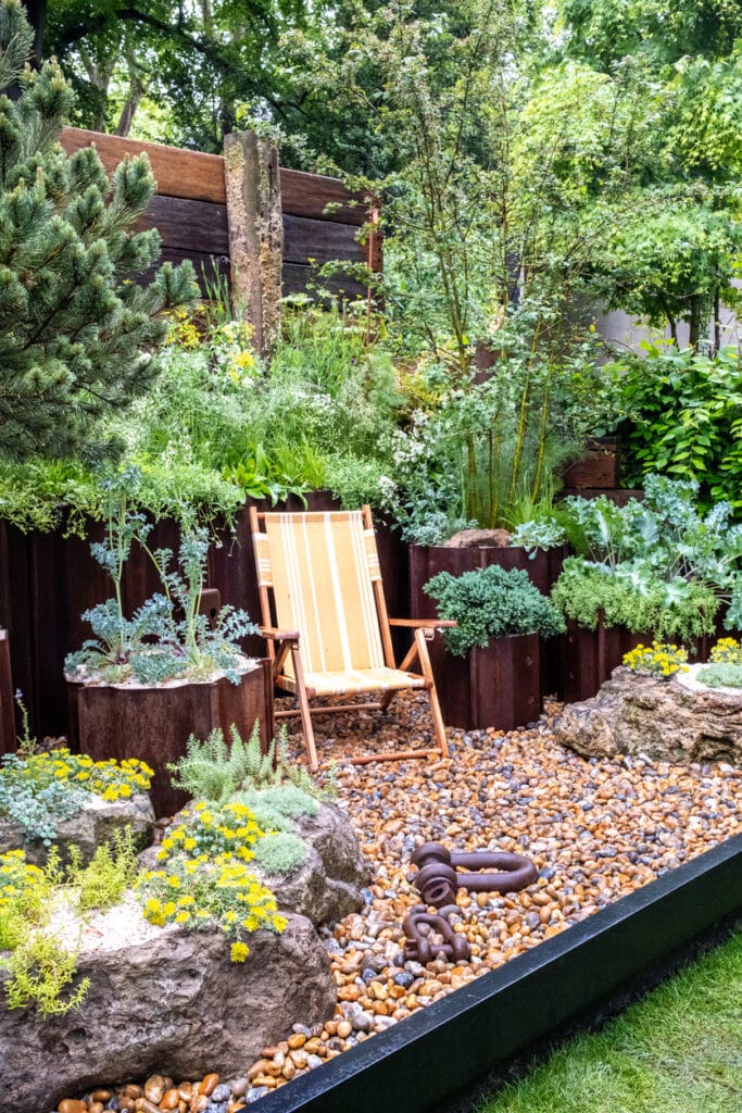 Gravel garden ideas with pots — striped deckchair beside raised planters and boulders on golden gravel, creating a low-maintenance seating nook.