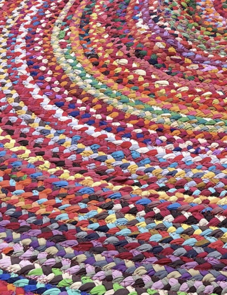 Close-up of colourful braided rag rug showing multicolour fabric strands woven into a circular pattern.