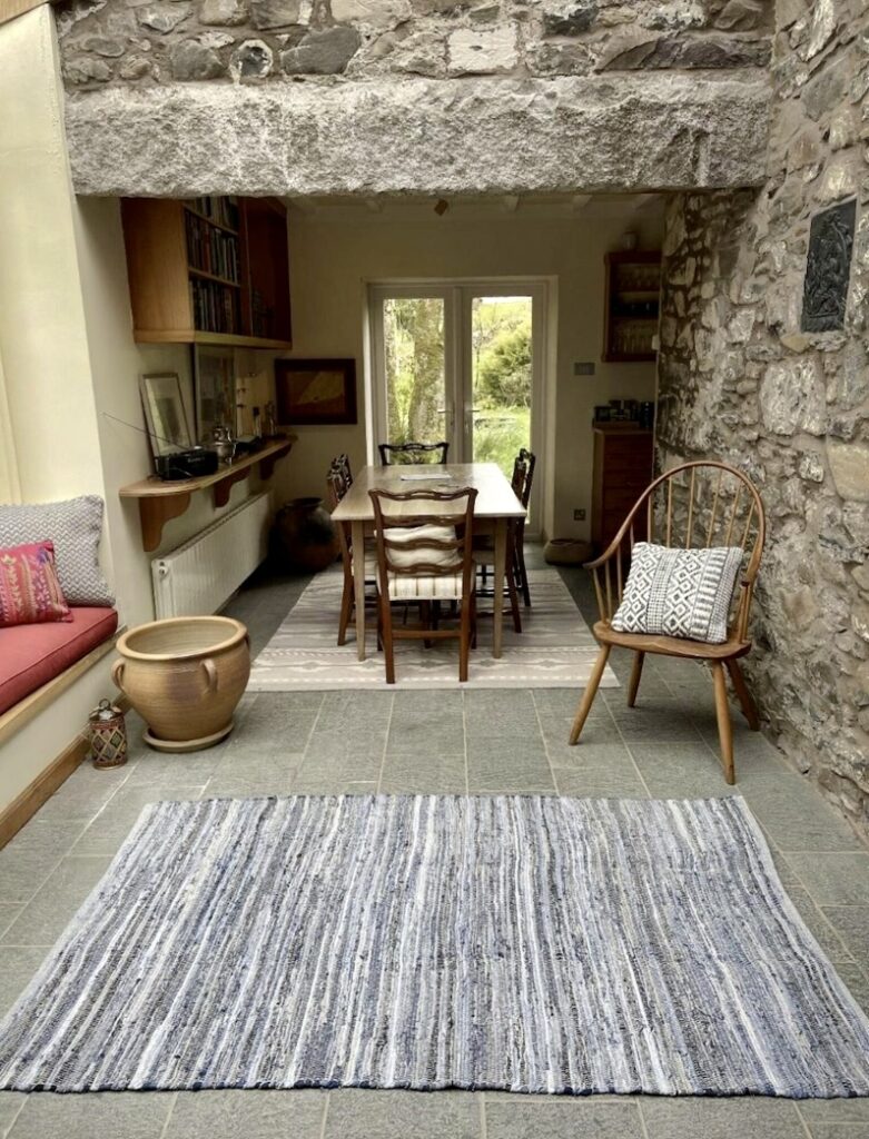 Denim rag rug placed in a stone-walled dining space with rustic wooden accents and a mid-century modern chair.