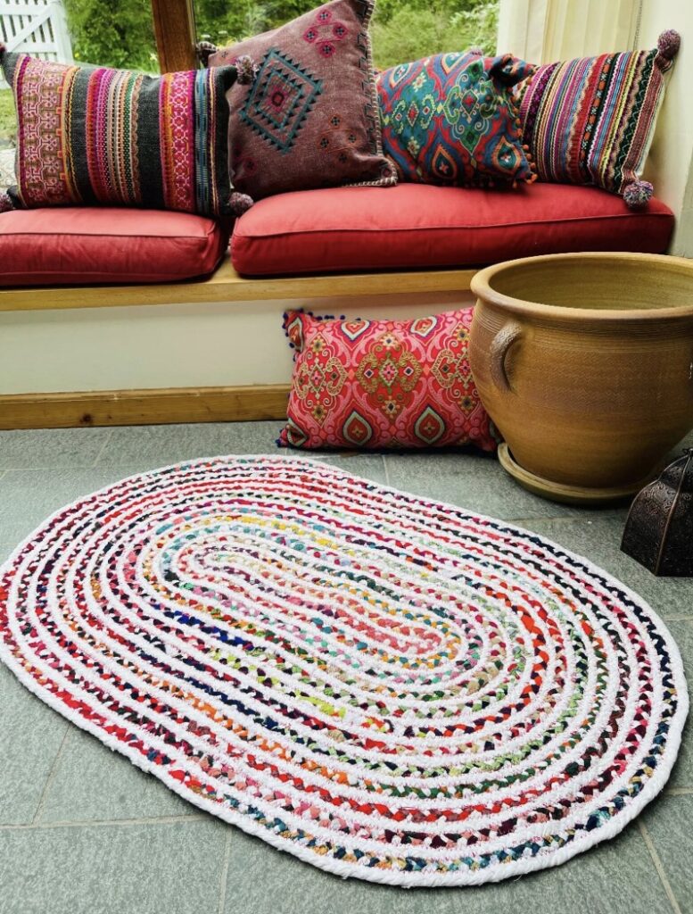 Carnival oval rag rug in a colourful boho seating nook with patterned cushions and large terracotta pots.