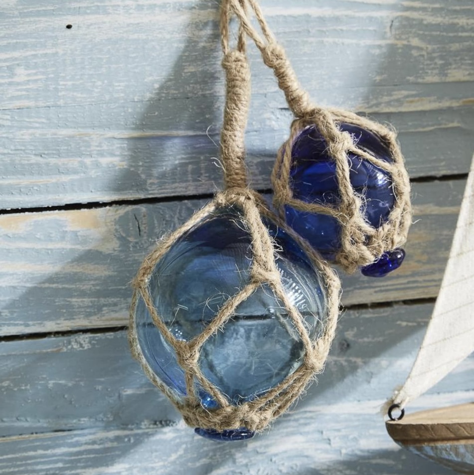 Set of two blue glass floats wrapped in jute rope, styled on a distressed coastal blue background
