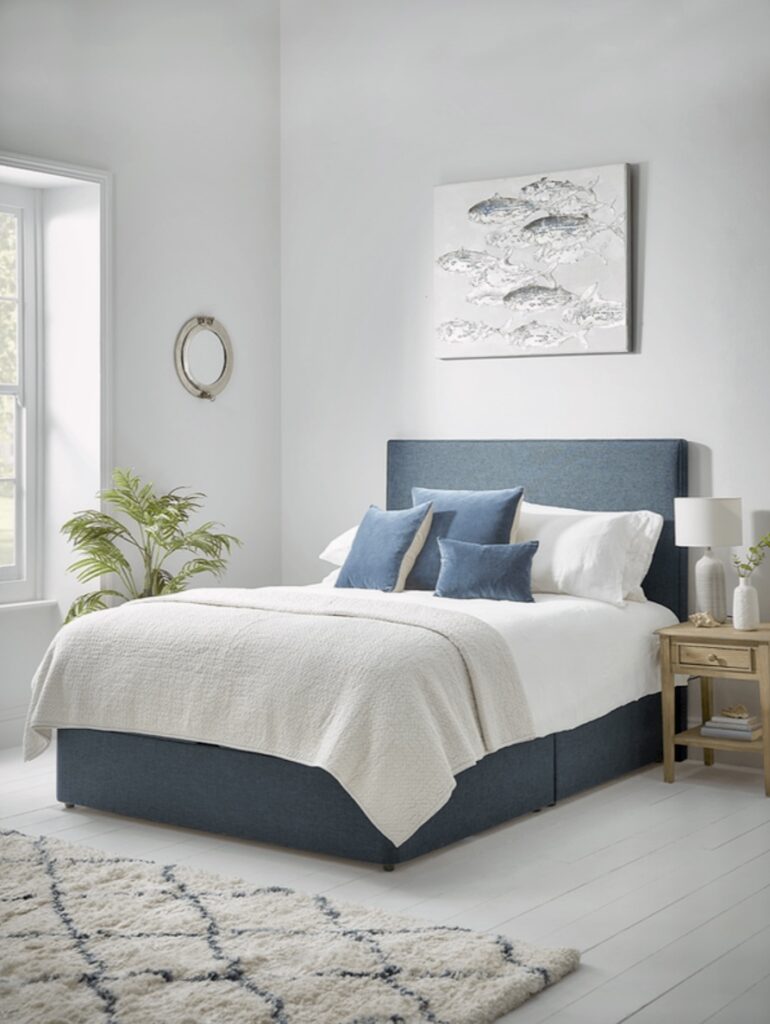 Coastal bedroom with navy upholstered bed, quilted cream bedding, and textured wall art in a seaside-inspired palette