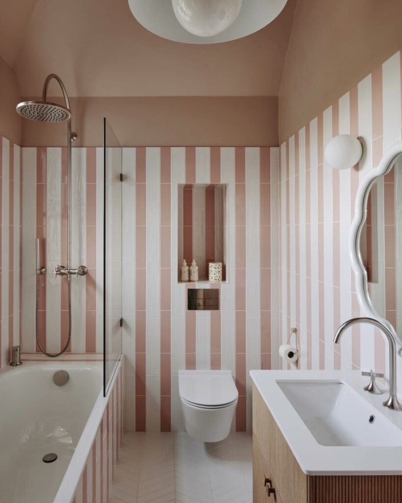 Small pink bathroom with Farrow & Ball Setting Plaster, vertical striped pink tiles, brass shower fittings and a wall-hung basin