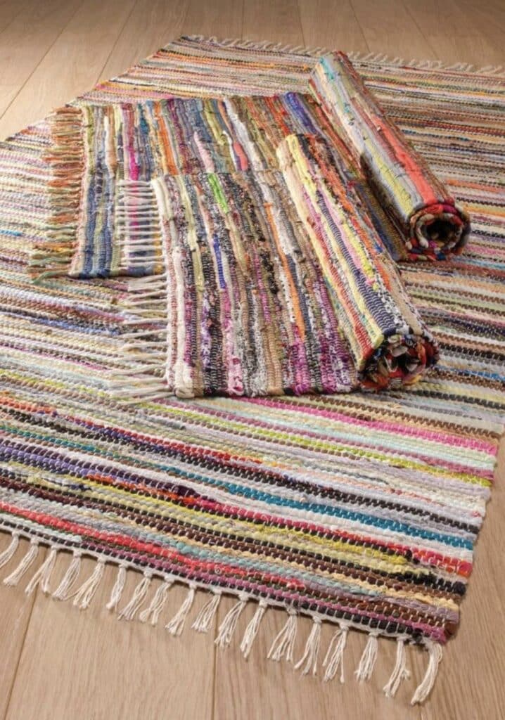 Handwoven rag rug with multicolour stripes and fringe on a wooden floor
