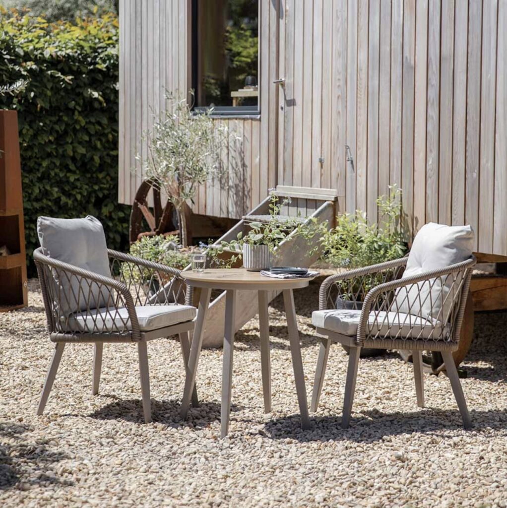 Atkin and Thyme outdoor seating set with rope chairs and gravel base beside a timber-clad house – gravel garden ideas with pots