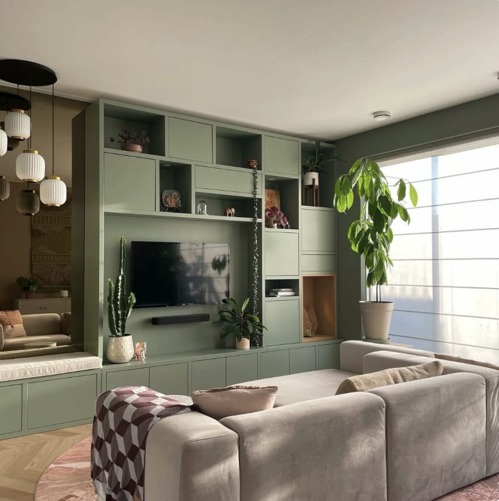 Green built-in shelving feature wall with a TV and storage cabinets in a small living room, with a sofa facing the unit.