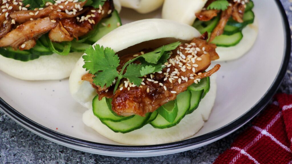 Hoisin chicken bao buns filled with sticky shredded chicken, cucumber, sesame seeds and fresh coriander — soft, fluffy, and full of flavour.