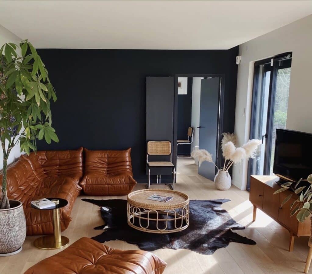 Modern retro interior design living room with a tan leather sofa against deep blue walls and vintage teak furniture.