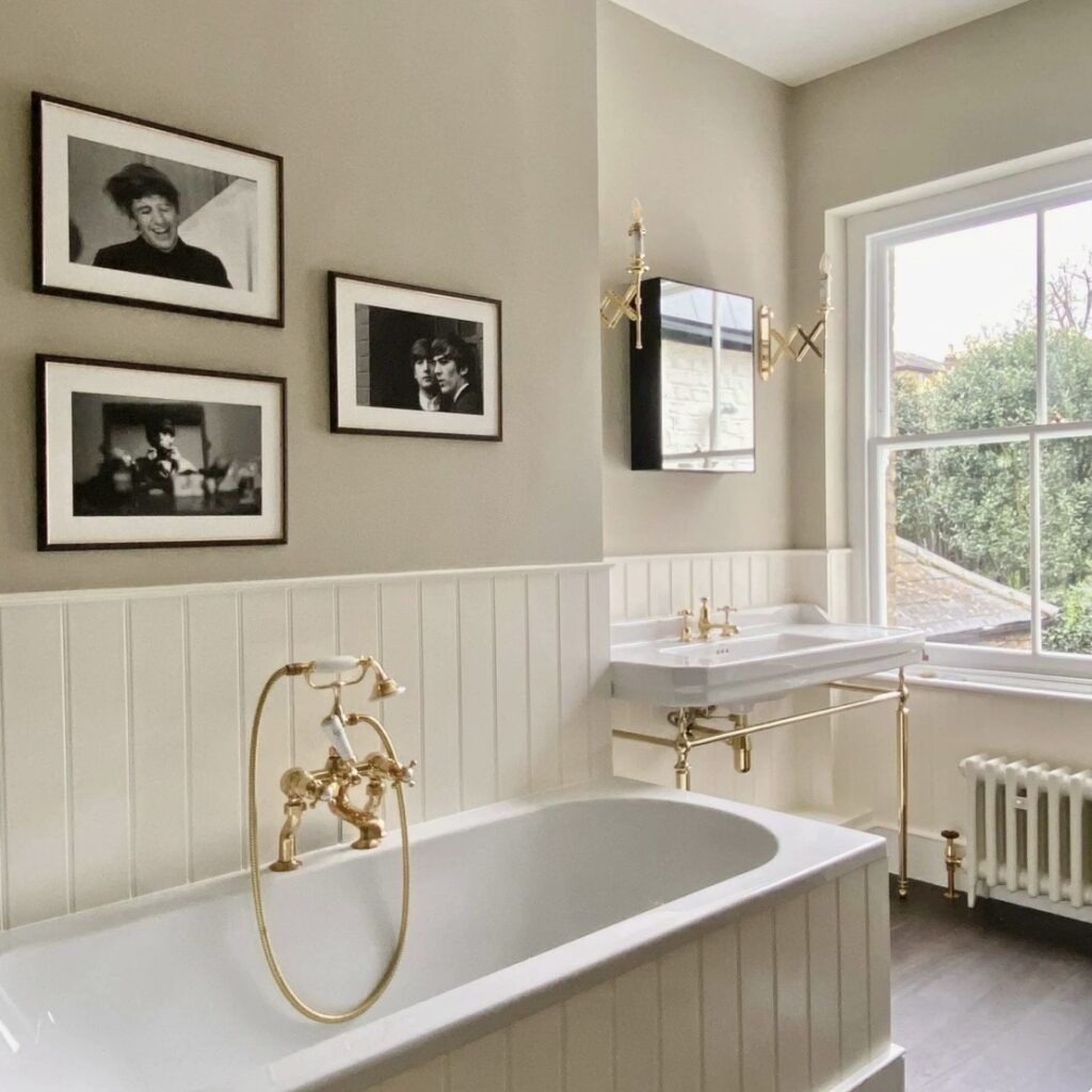 Oat neutral bathroom ideas with Farrow & Ball Old White, panelled bath, brass taps and wall lights, and a traditional basin by the window.