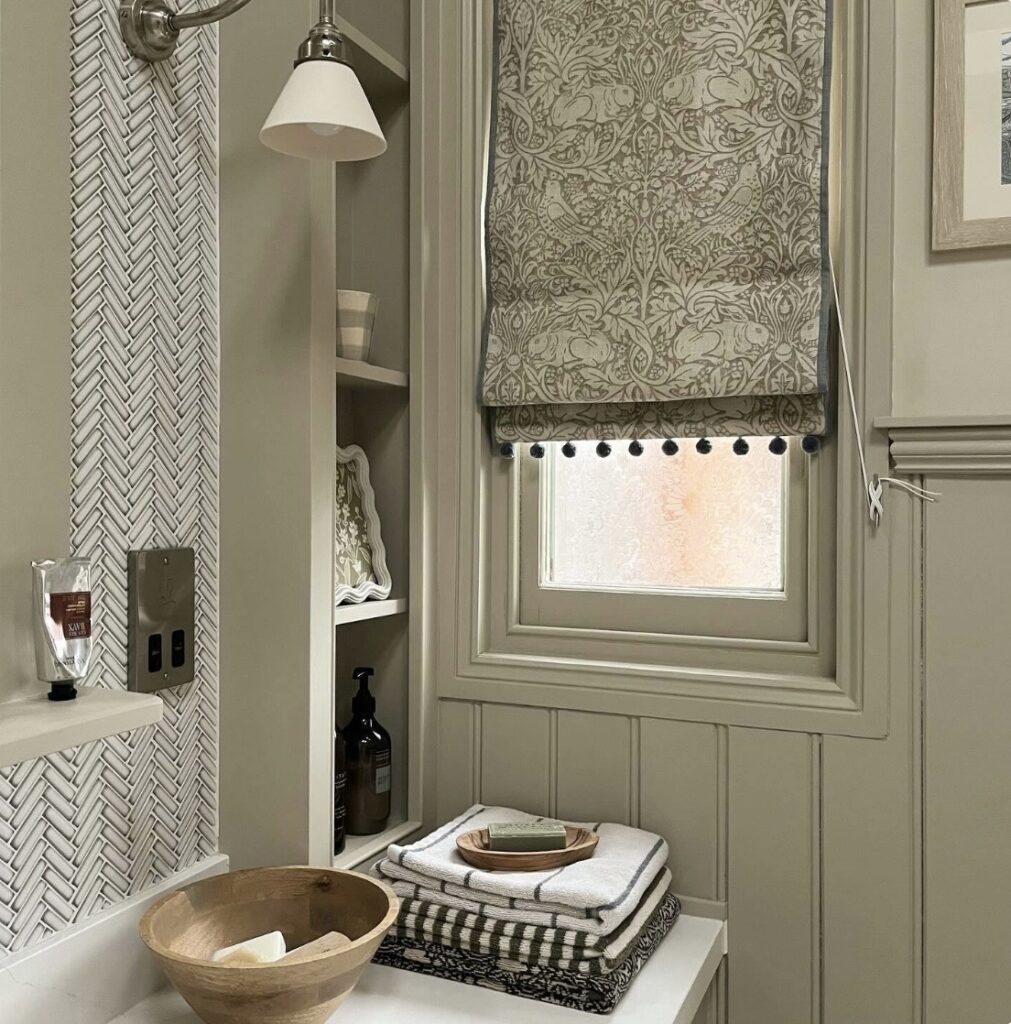 Neutral bathroom ideas in soft greige with herringbone neutral bathroom tiles, a patterned roman blind, and Farrow & Ball Drop Cloth and Shaded White paint.