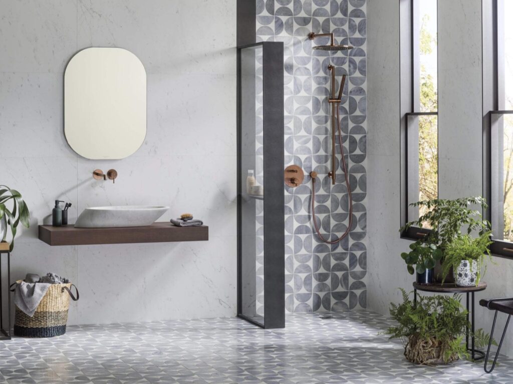 Retro grey neutral bathroom ideas with Porcelanosa Figure Spiral Light geometric neutral bathroom tiles, minimal vanity, and warm metal shower fittings.