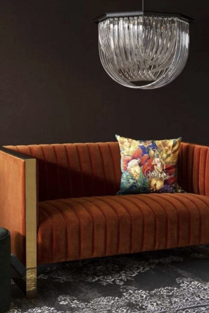Burnt orange velvet retro sofa with floral cushion and crystal chandelier