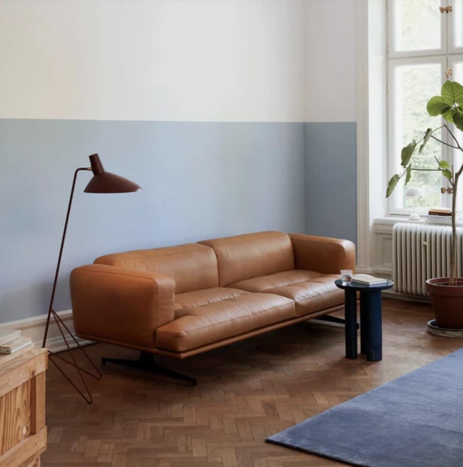 modern living room with tan leather sofa, dusty blue half-painted walls and a navy rug