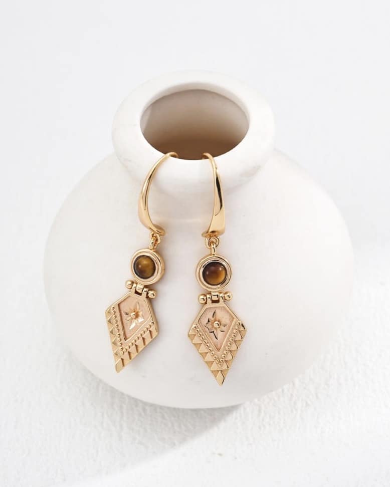 Gold tiger’s eye geometric drop earrings on a white vase