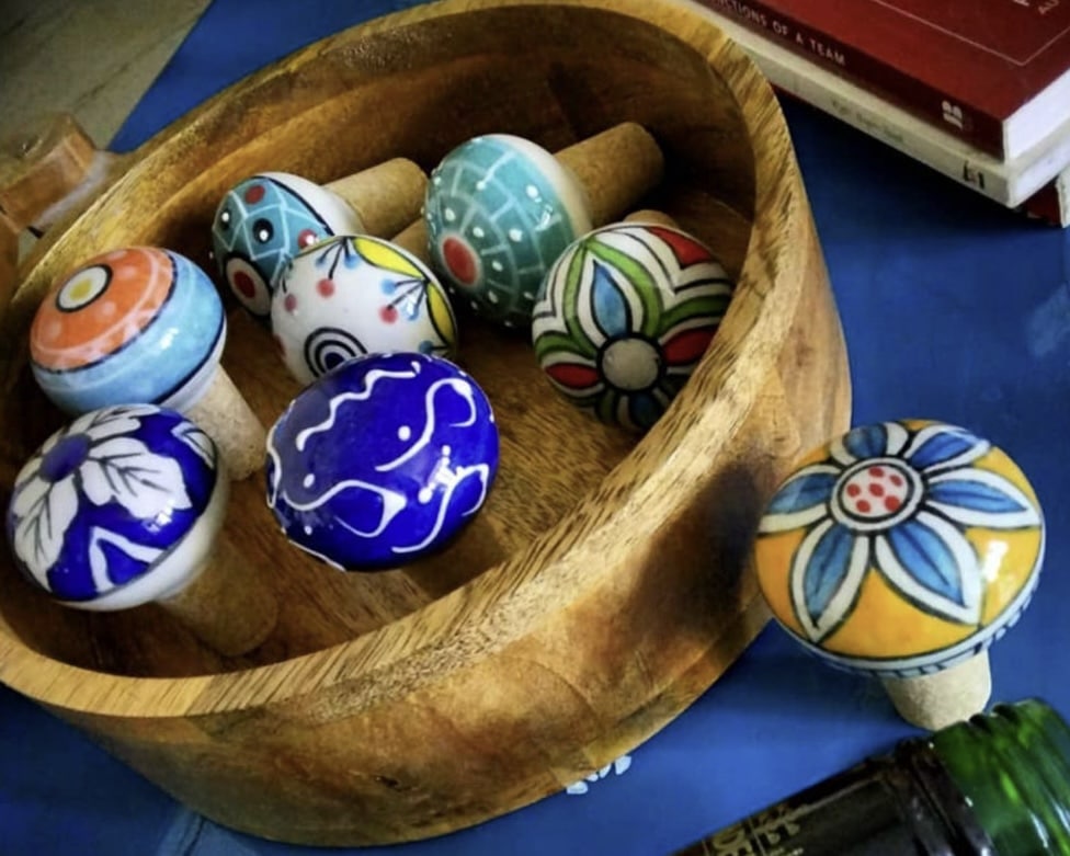 Colourful ceramic wine bottle stoppers in a wooden bowl