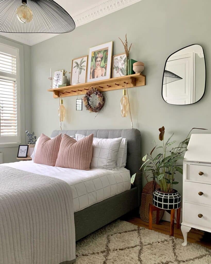 Small bedroom storage ideas — oak peg rail shelf above bed in Farrow & Ball Cromarty bedroom with prints, mirror and botanical pendant light