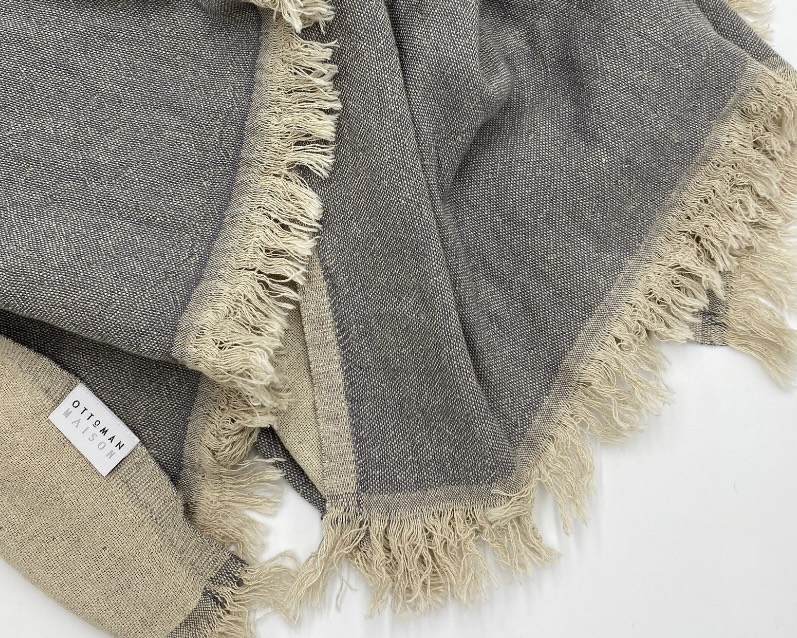 Puglia linen and cotton blend blanket draped over neutral bedding in soft grey and oatmeal tones