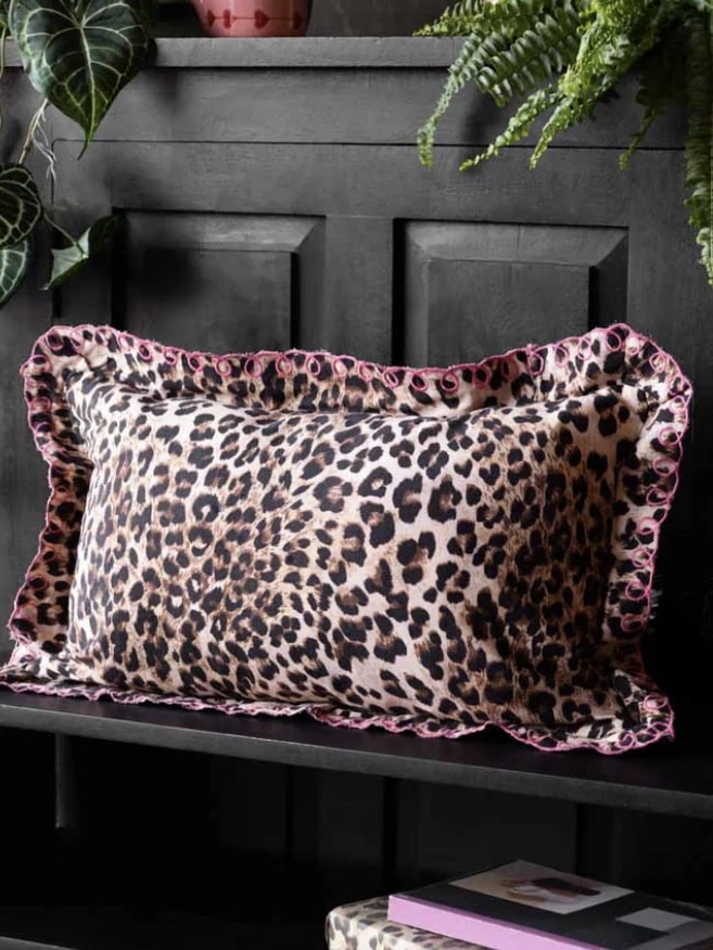 Leopard print cushion with pink scalloped edge on a dark shelf