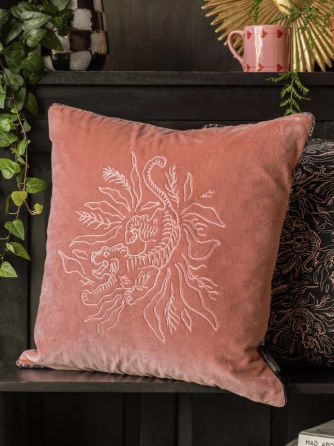 Pink velvet embroidered tiger cushion on a dark shelf