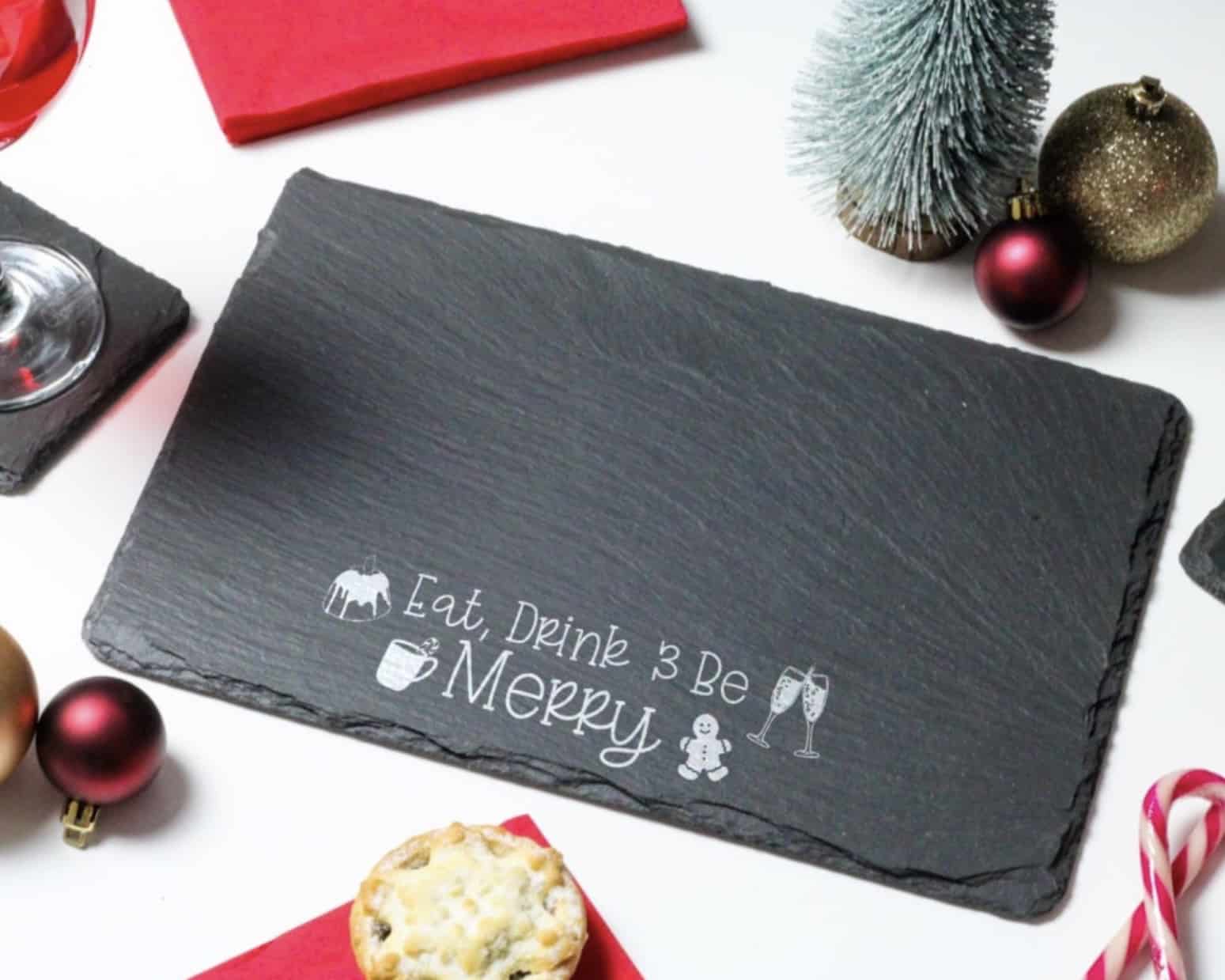 Festive slate cheeseboard engraved with Eat, Drink and Be Merry surrounded by Christmas decorations